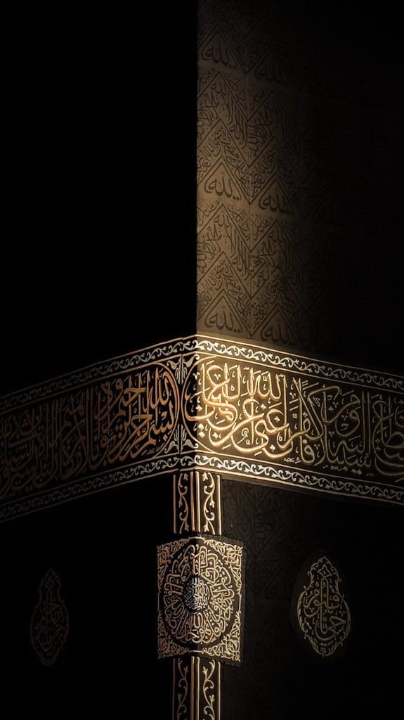 The black Kiswah covering the Kaaba in Mecca, with gold embroidered Arabic calligraphy along a corner illuminated by focused light.